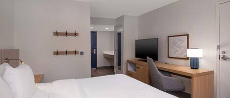 A hotel room with a bed, desk, chair, TV, lamp, and a door.