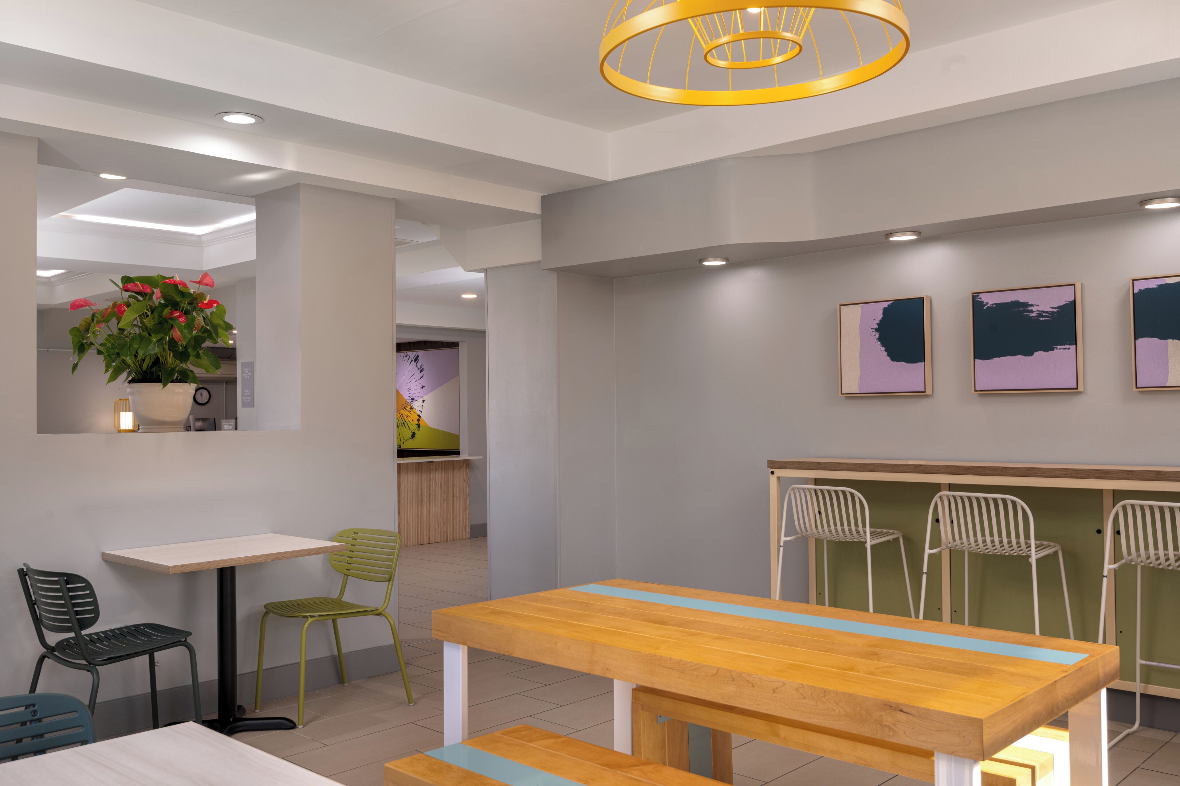 A modern dining area with a wooden table and chairs, a potted plant, and artwork on the wall.