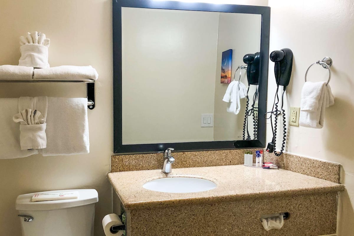 Un baño con lavamanos, espejo, toallero y retrete.