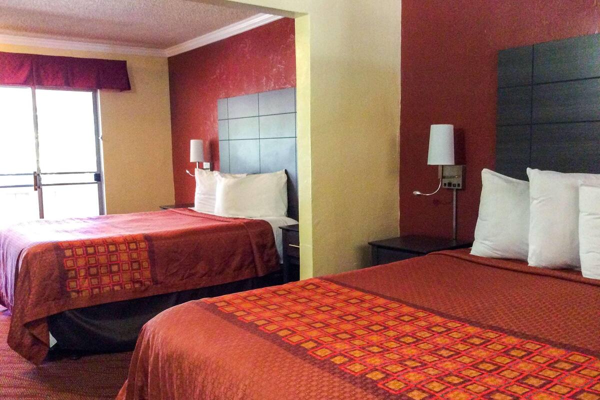 A hotel room with two beds, each with a headboard and a bedside table.