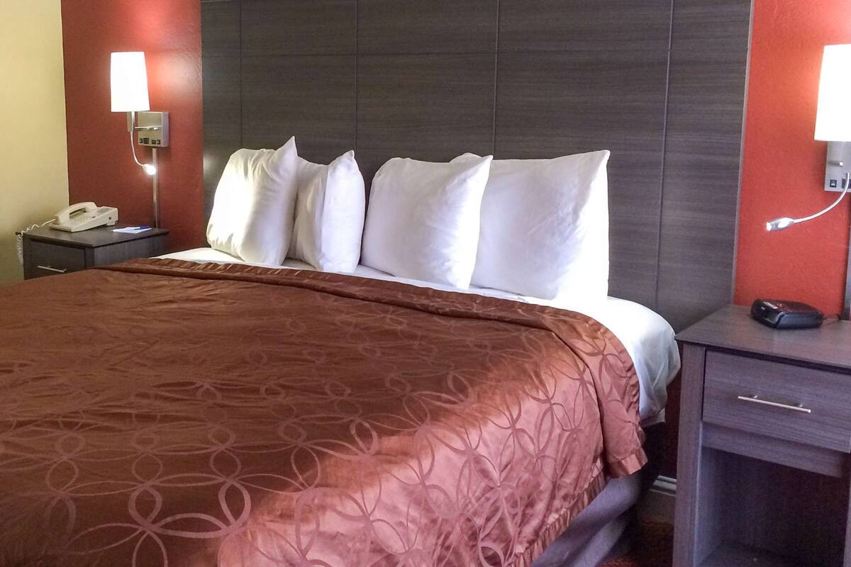 A hotel room with a large bed, a bedside table with a phone, and a nightstand with a lamp.