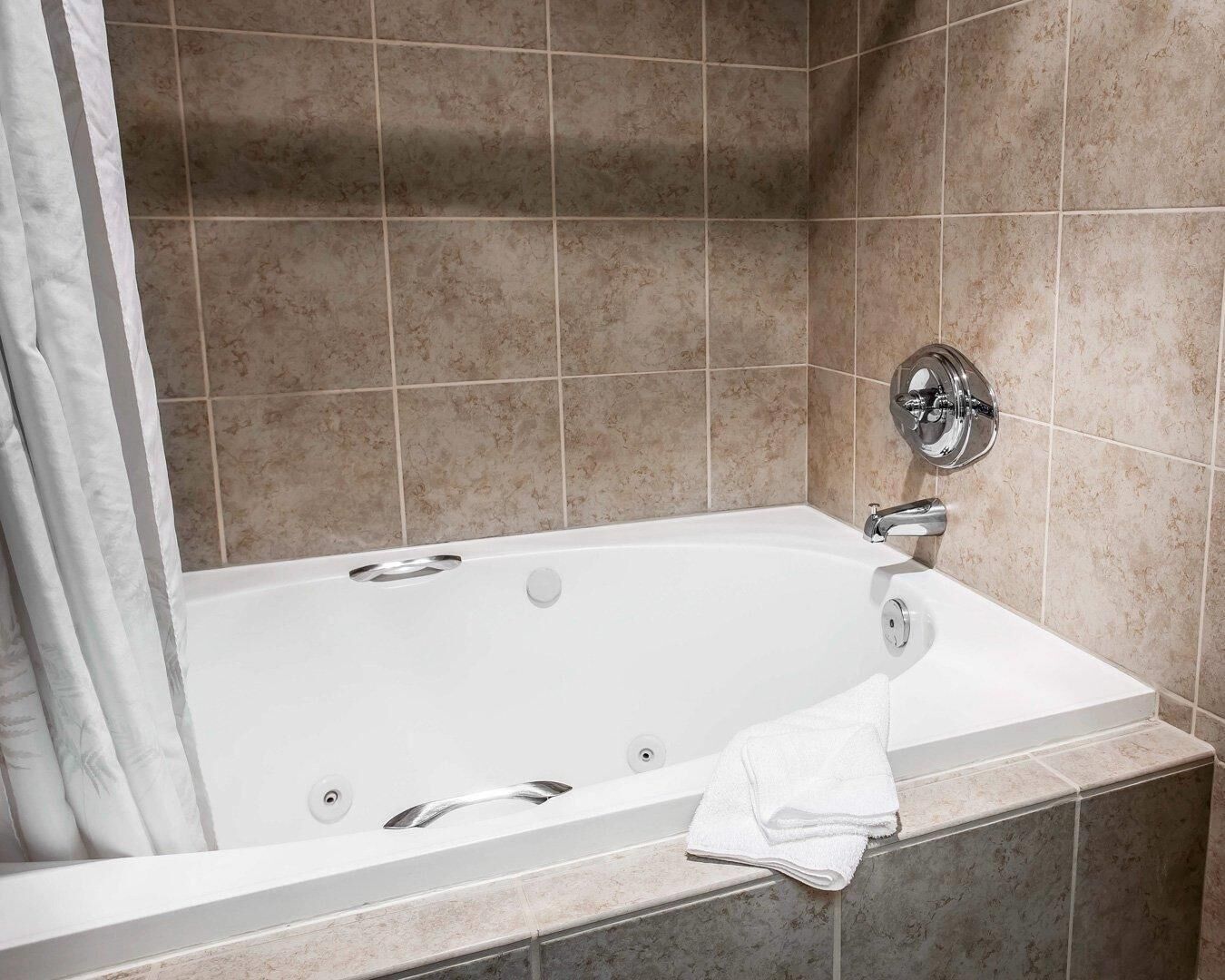 Una bañera blanca con grifería de cromo, una toalla y una cortina en un baño con azulejos.
