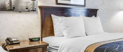 A hotel room with a bed, two bedside lamps, a nightstand with a phone, a digital clock, and a framed picture on the wall.