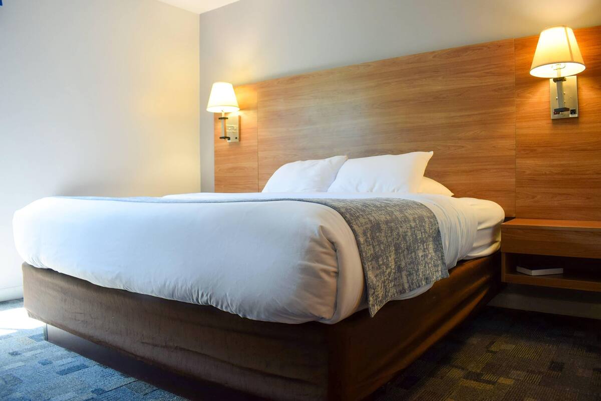 A neatly made bed with a wooden headboard, two bedside lamps, and a small bedside table.