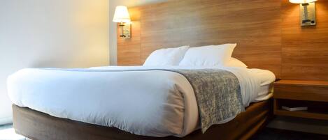 Una cama bien hecha con cabecera de madera, dos lámparas de noche y una mesita auxiliar.