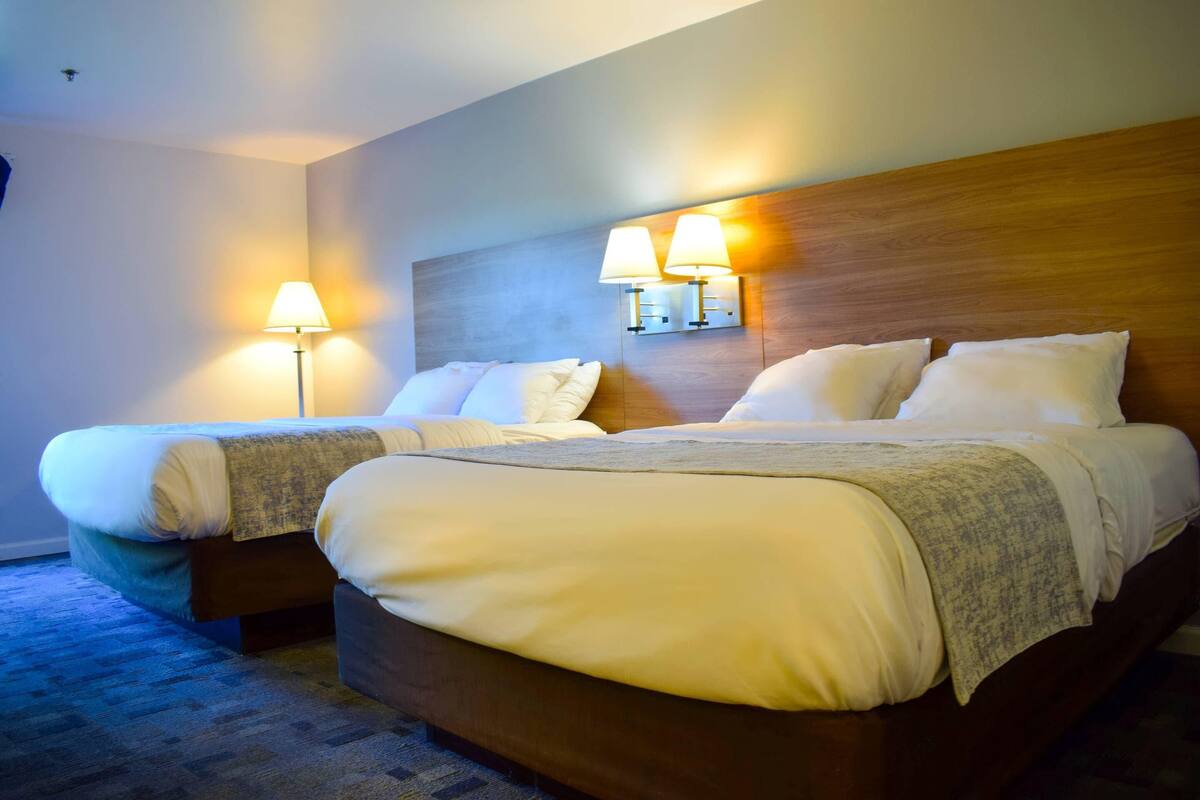 A hotel room with a double bed, two bedside lamps, and a headboard with a light fixture.