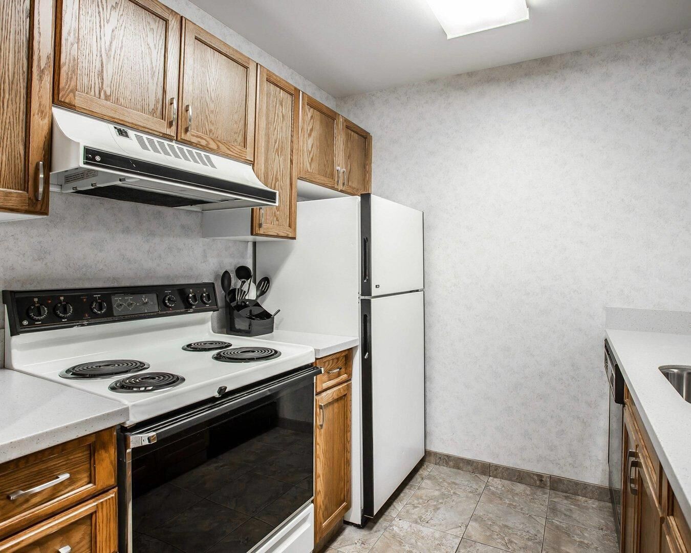 A kitchen with wooden cabinets, a white stove, a refrigerator, and a tiled floor.