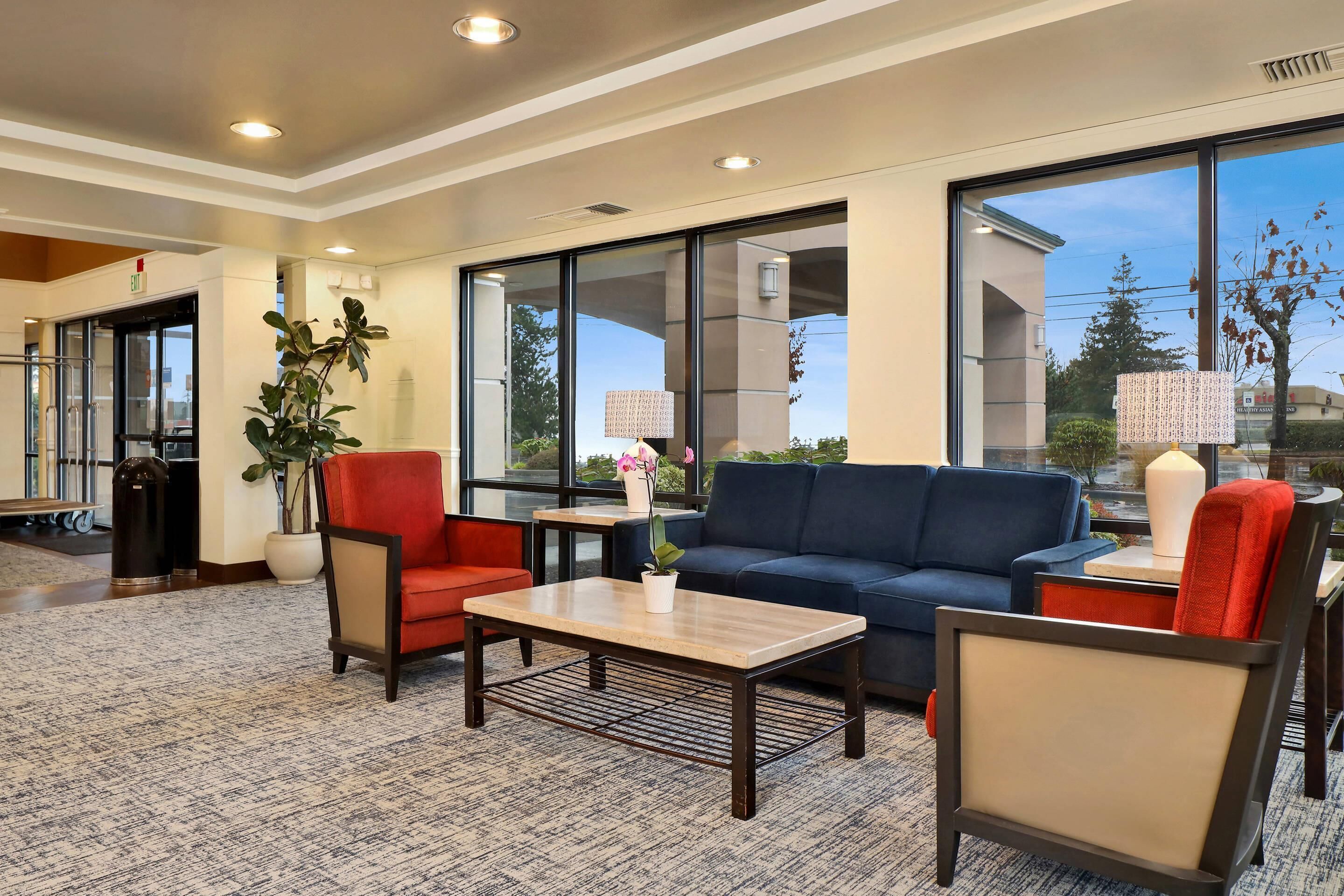A lobby with a sofa, chairs, a coffee table, a potted plant, and large windows.