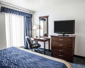 A hotel room with a bed, a desk, a chair, a dresser, a television, and a window with curtains.