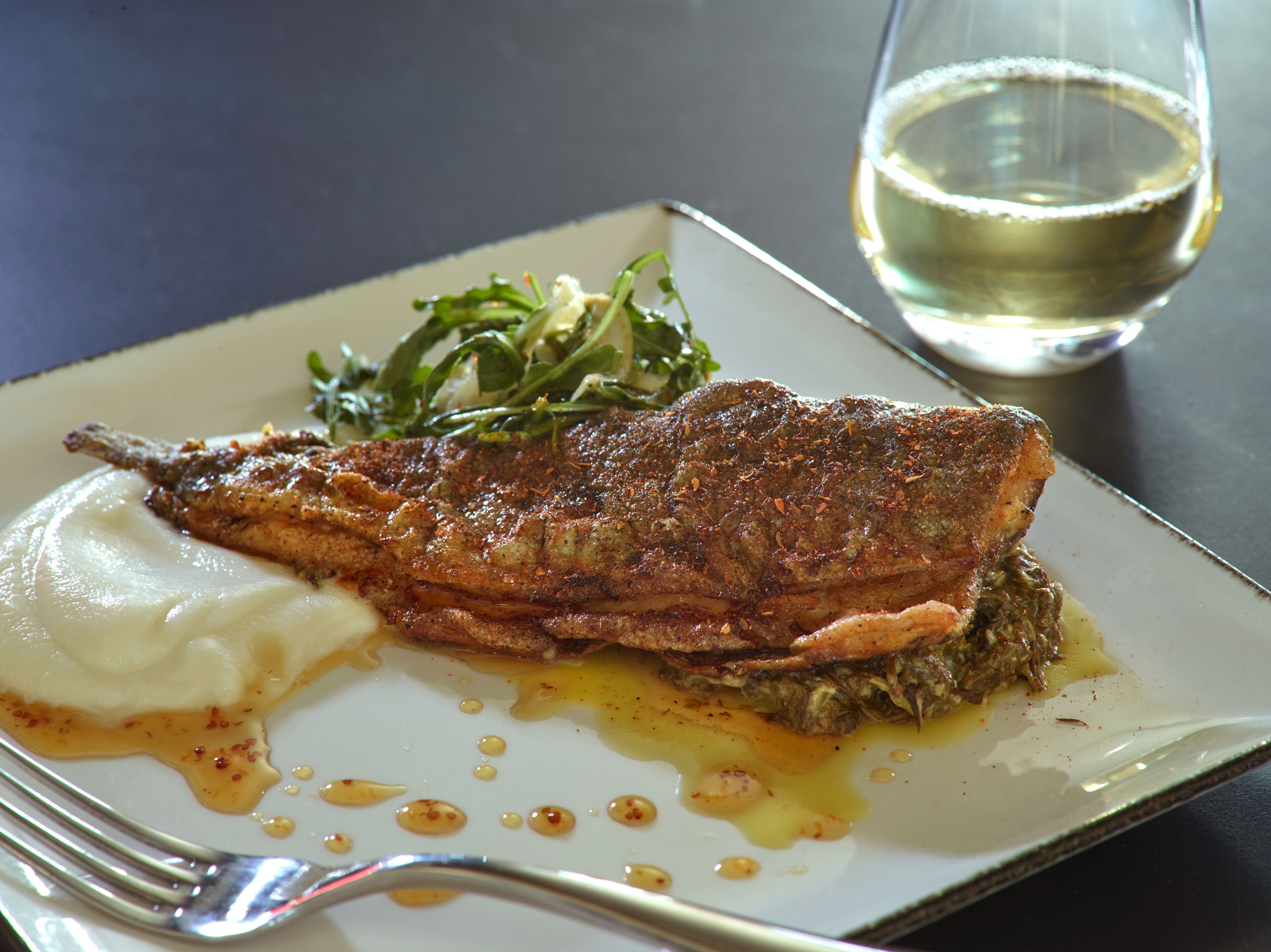 A plate with a grilled fish, mashed potatoes, and a green salad, accompanied by a glass of white wine.