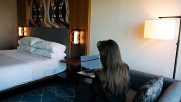 Een hotelkamer met een bed, een bureau met een laptop, een lamp en een schilderij aan de muur.