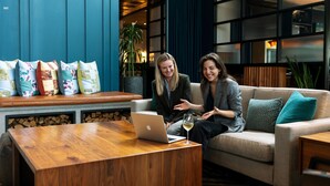 A modern lounge area with a wooden coffee table, a sofa with cushions, and a laptop on the table.