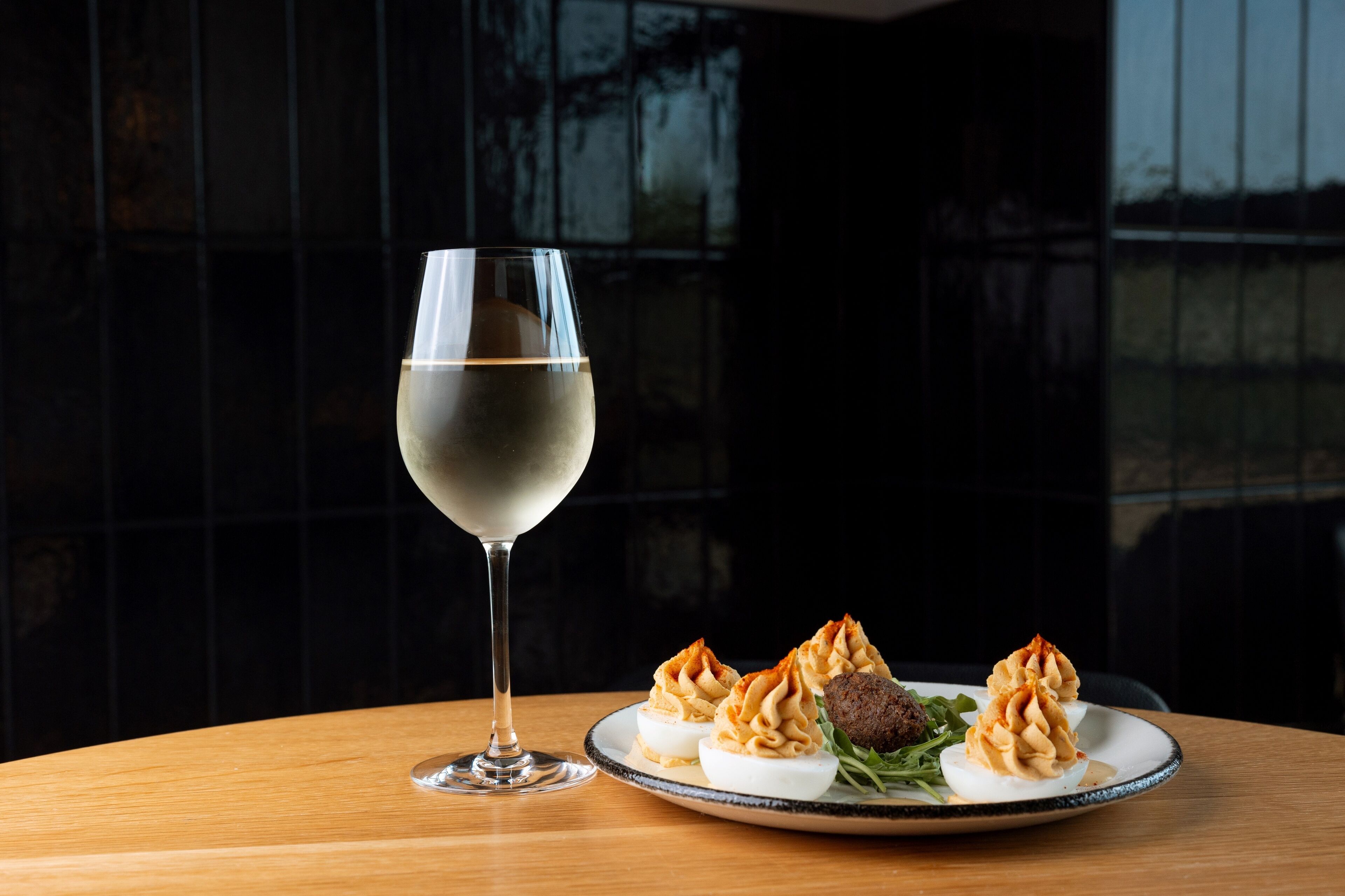 A plate of deviled eggs and a glass of white wine on a wooden table.