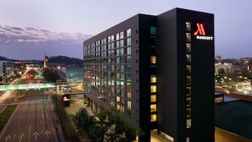 A modern Marriott hotel with a prominent 'M' logo, large windows, and a view of the surrounding cityscape at dusk.