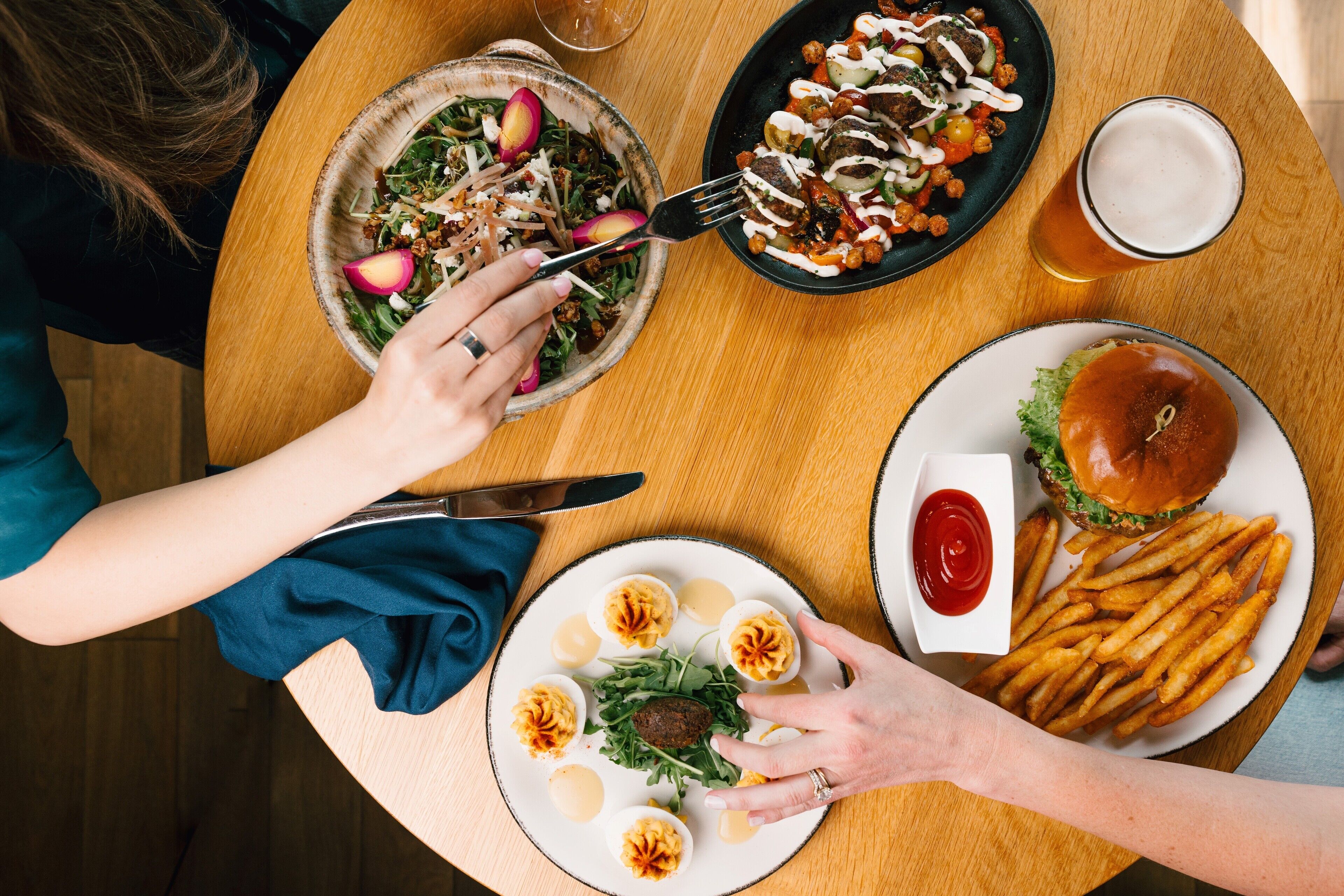 A dining table with a variety of food items including a salad, a burger, fries, and a drink.