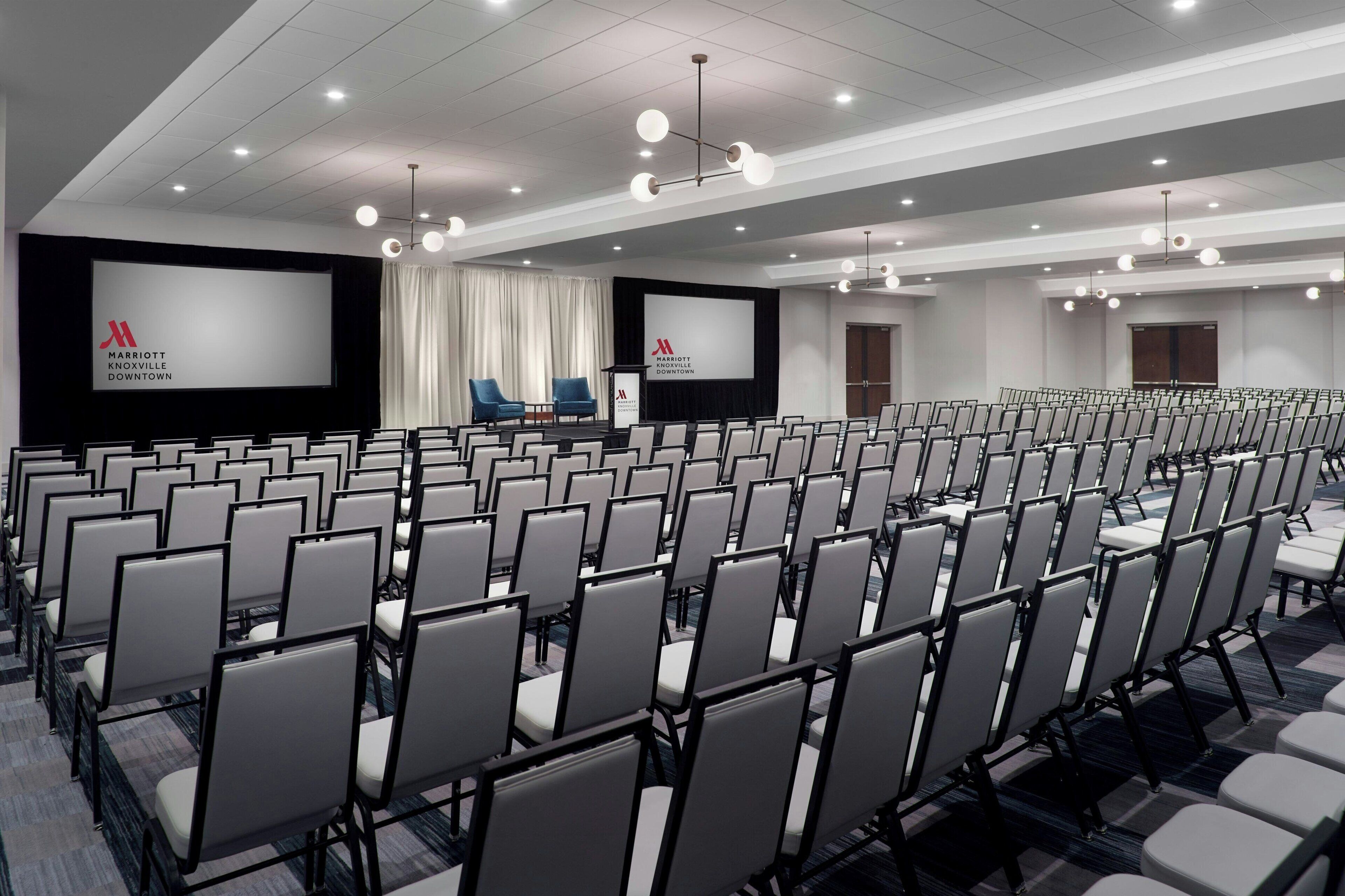 Un salón de conferencias con filas de sillas, una pantalla grande y un atril.