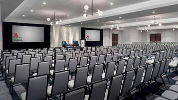 Un salón de conferencias con filas de sillas, una pantalla grande y un atril.