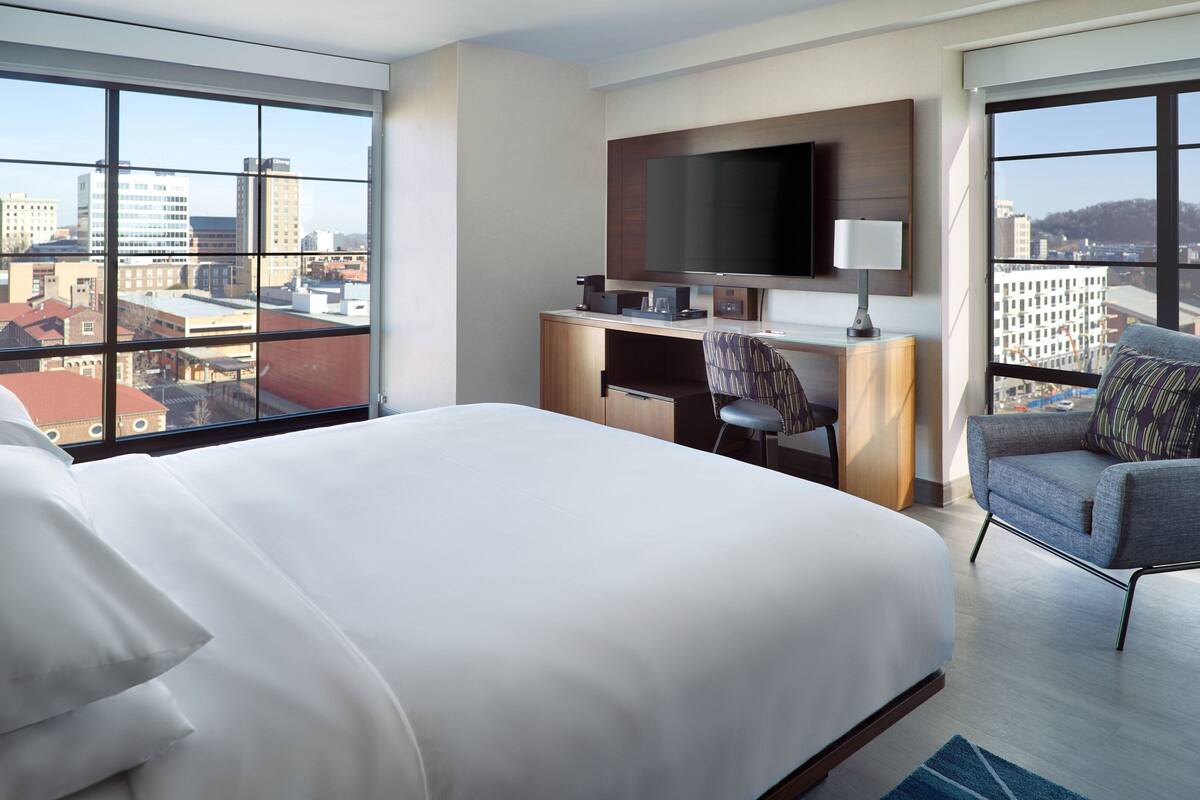 A hotel room with a large bed, a desk with a TV, and a view of the cityscape.