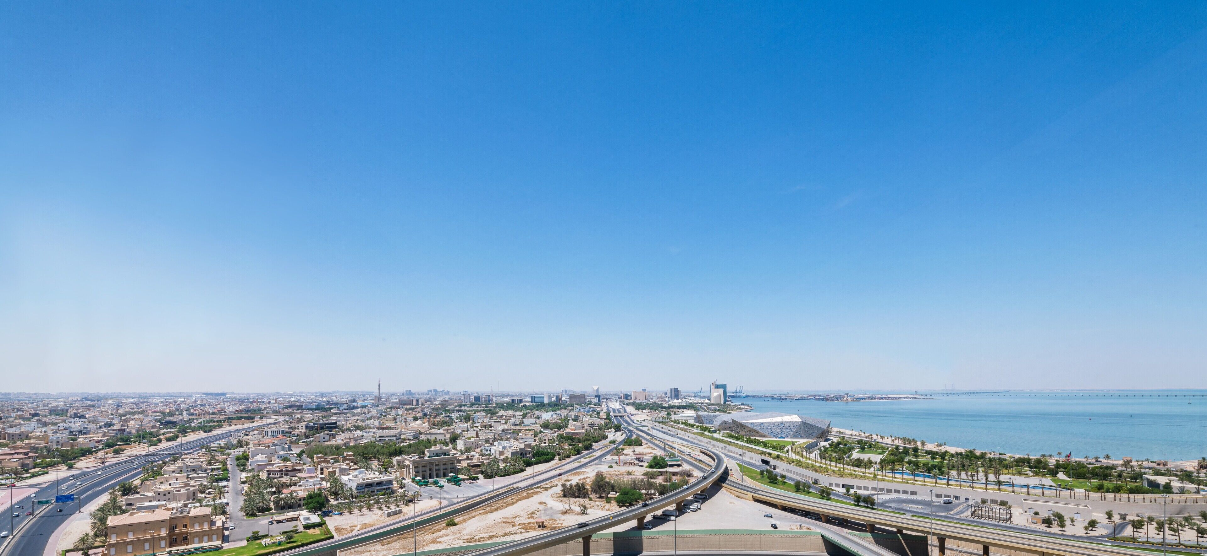 Panorama urbano con vista sul mare, che include un'autostrada, edifici moderni e un ponte.