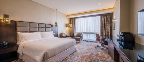 A hotel room with a large bed, a desk, a chair, a TV, and a view of the outdoors.
