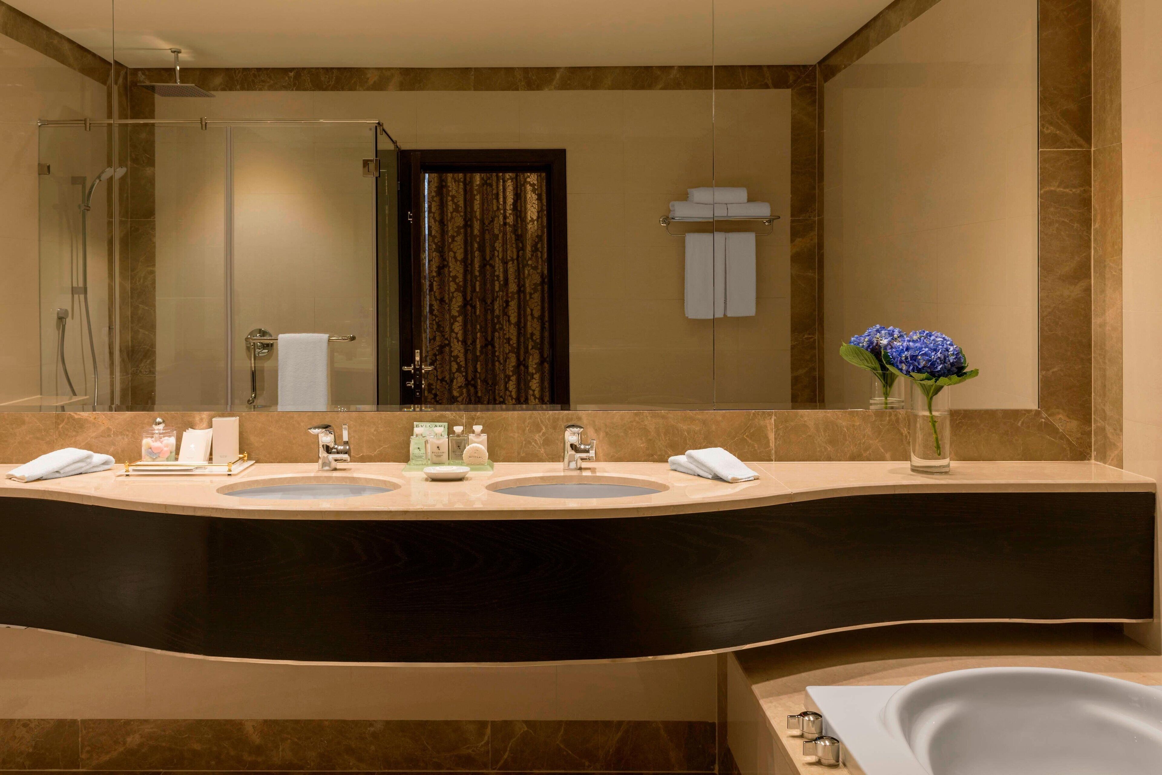 A modern bathroom with a curved vanity, two sinks, a large mirror, a shower area, and a bathtub.
