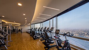 Ein Fitnessraum mit Cardiogeräten und Gewichten, große Fenster mit Blick auf die Stadt.
