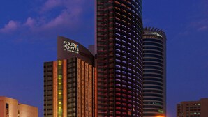 Ein Hochhaus-Hotel mit einem gut sichtbaren Schild "Four Points by Sheraton“, umgeben von anderen Gebäuden und einer belebten Straße im Abenddunst.
