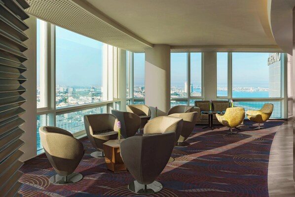 A modern lounge with large windows, comfortable seating, and a view of the city.