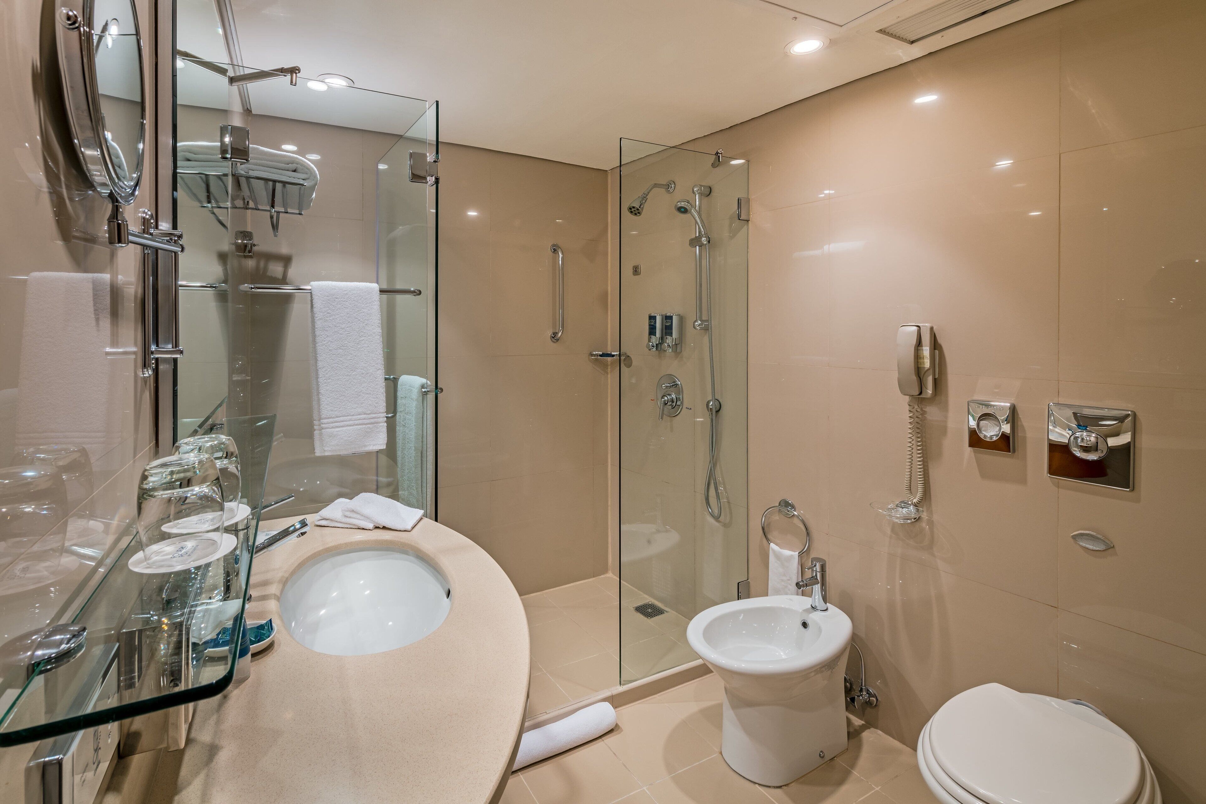 A modern bathroom with a glass-enclosed shower, a glass-topped sink, a bidet, and a toilet.