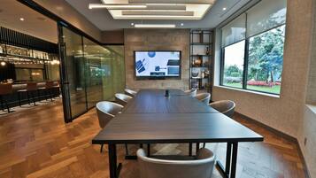 Un salón de conferencias con una mesa larga, sillas, una pantalla de televisión y una zona de bar con taburetes.