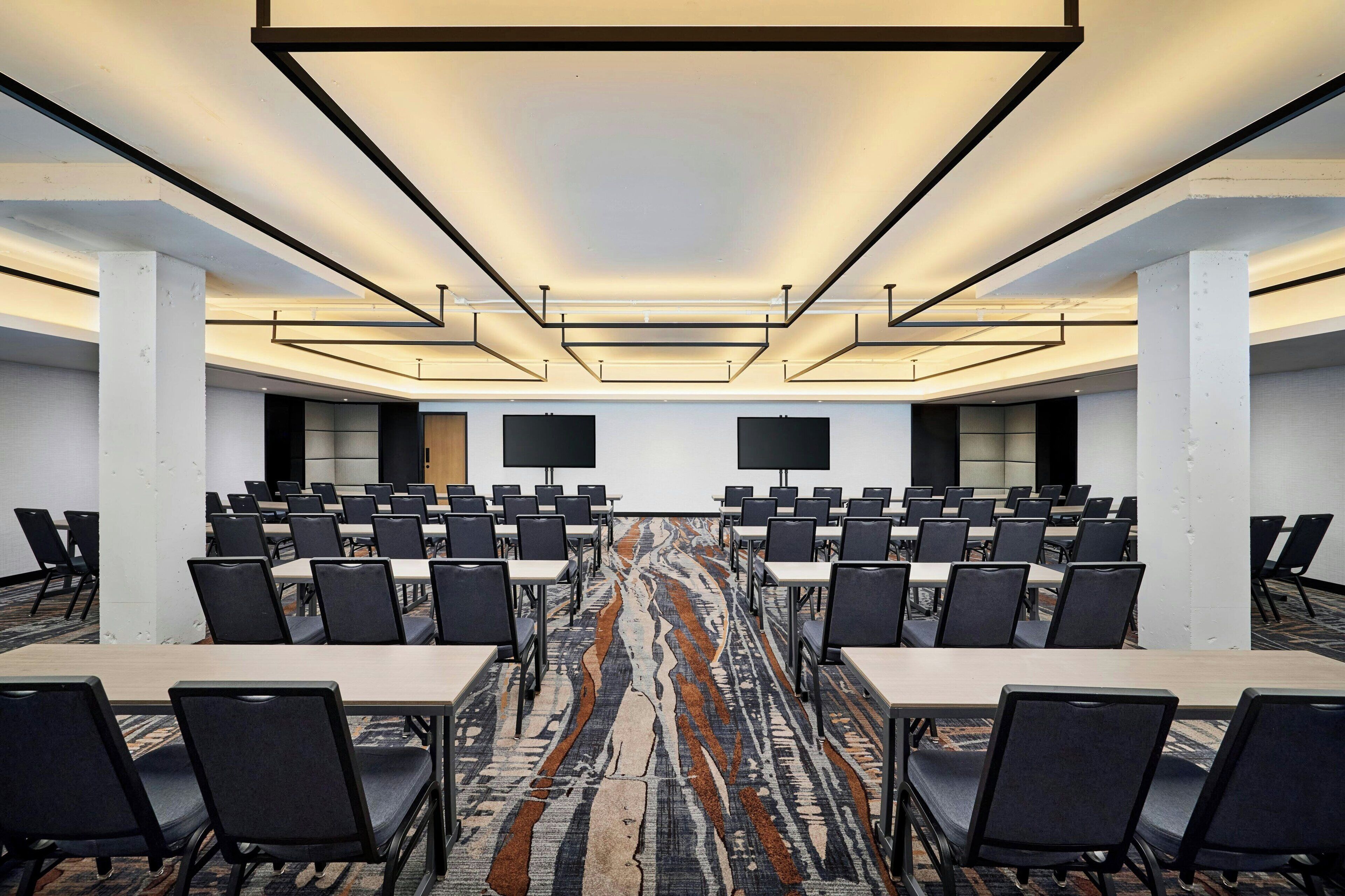 Une salle de conférence avec des rangées de tables et de chaises, une moquette à motifs et un plafond au design moderne.