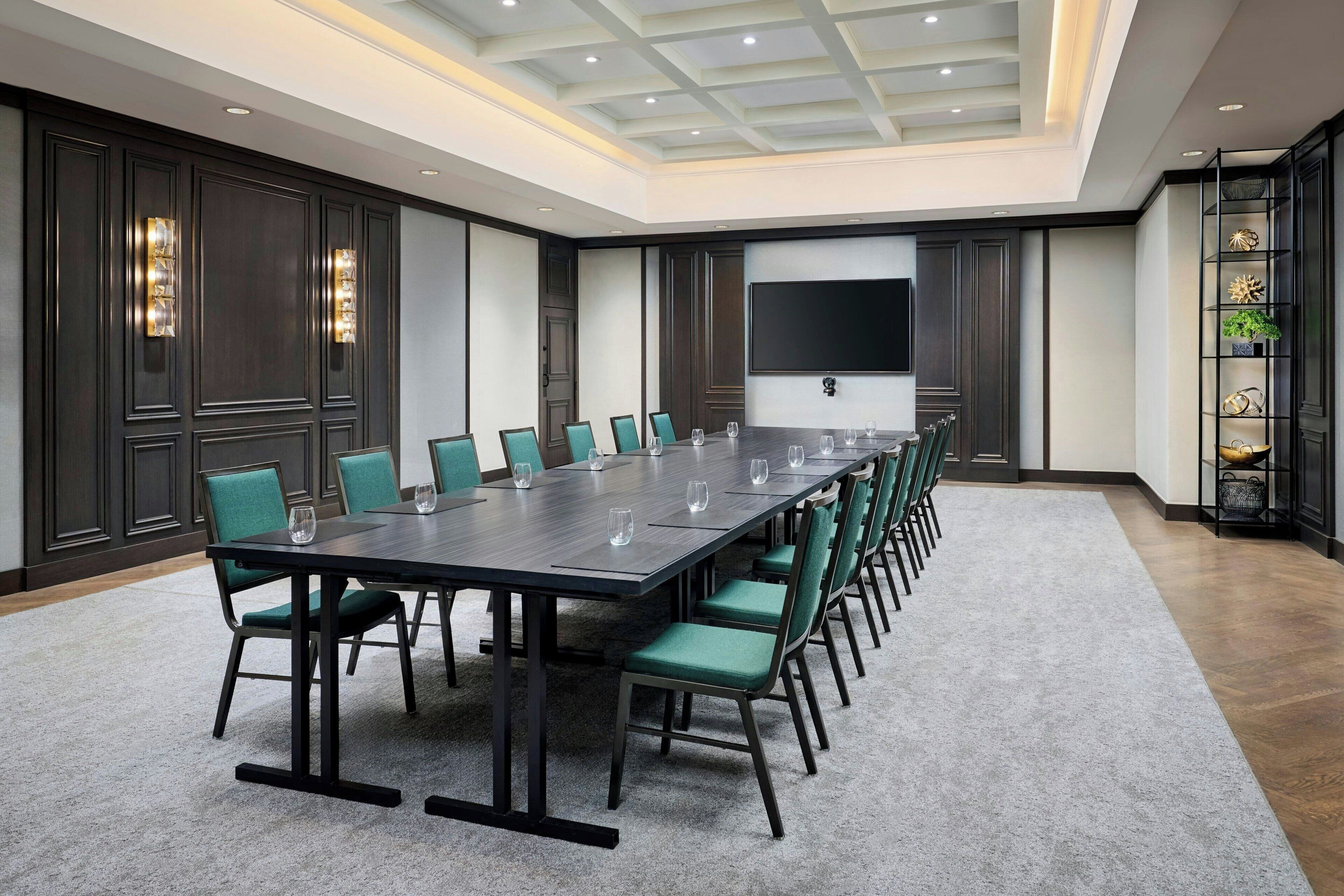 A conference room with a long table, green chairs, and a large screen on the wall.