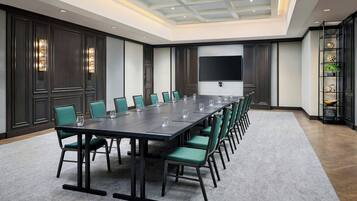 A conference room with a long table, green chairs, and a large screen on the wall.
