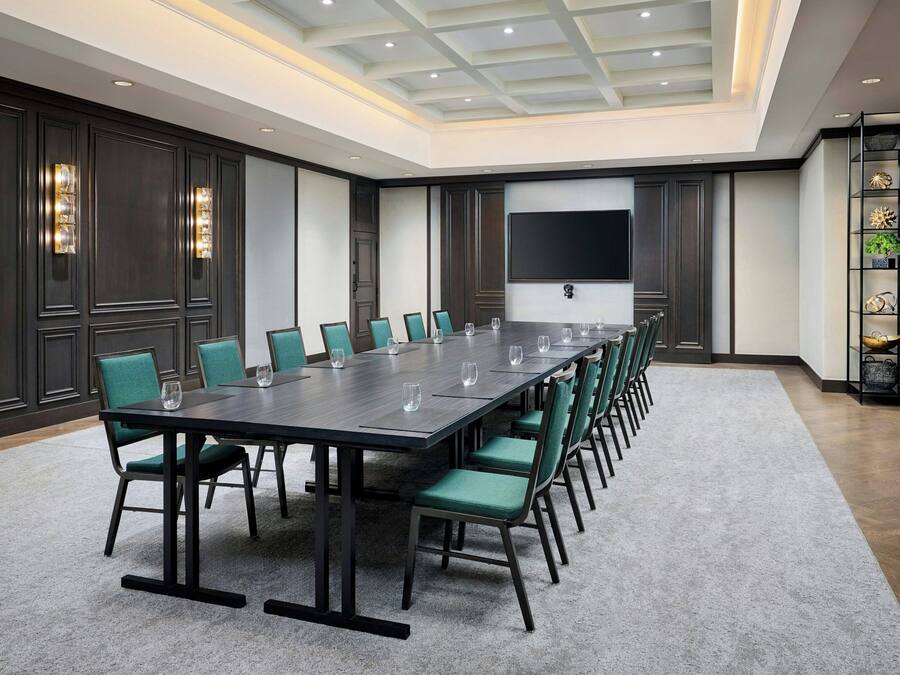 A conference room with a long table, green chairs, and a large screen on the wall.