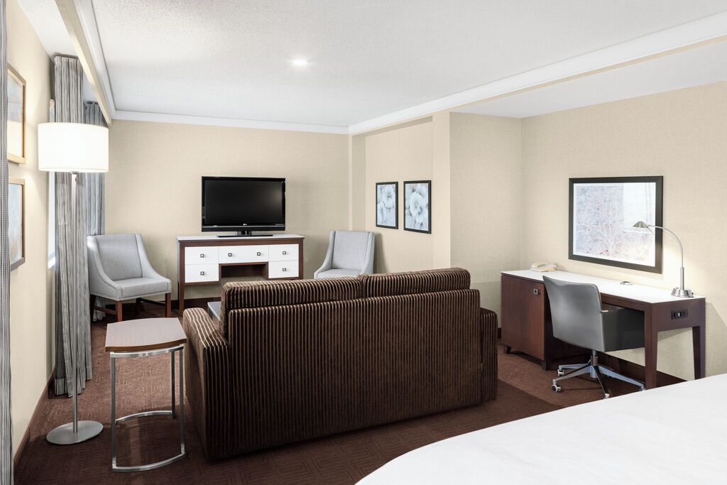 Habitación de hotel con cama, escritorio, televisión, dos sillas, un sofá y una mesita.