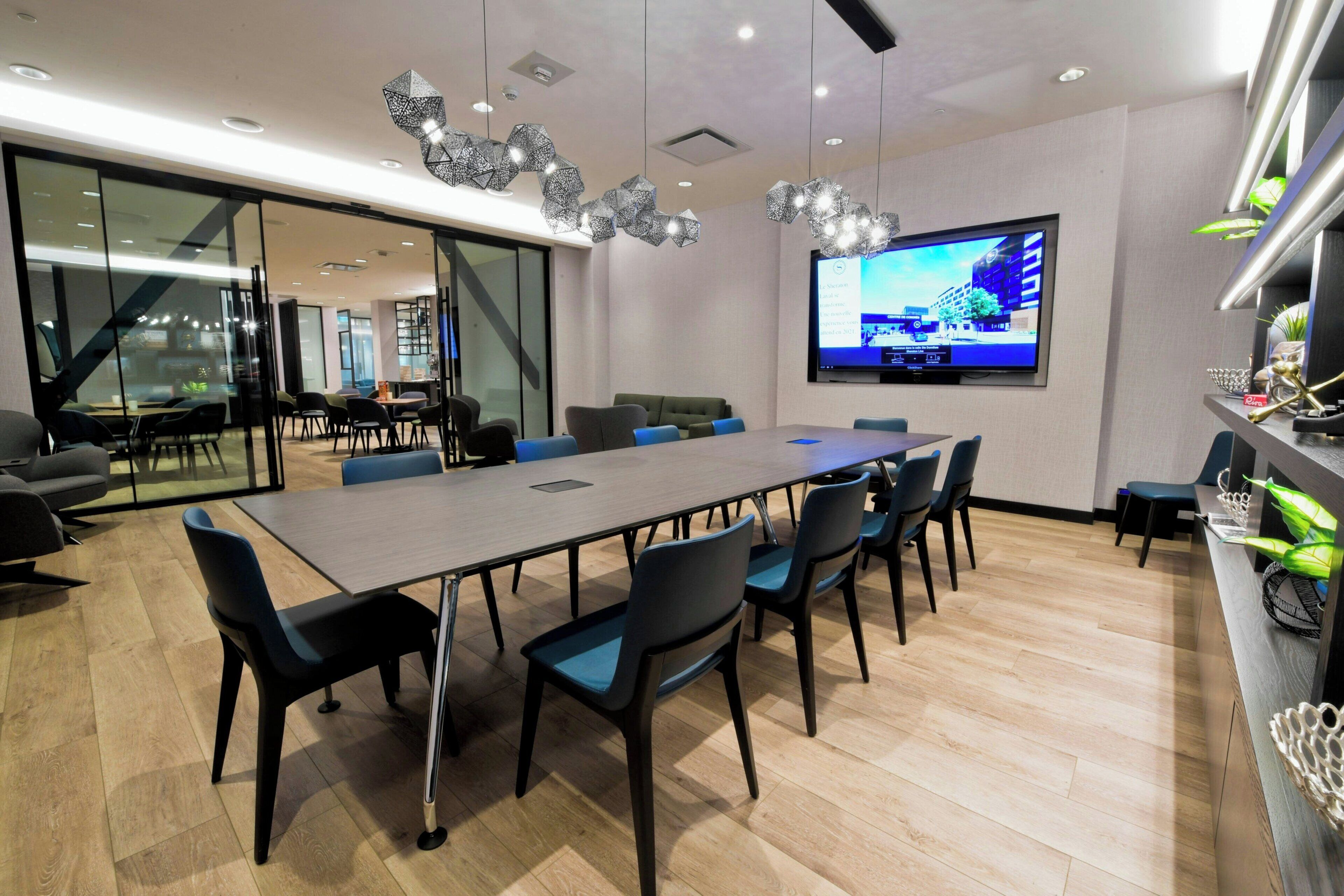 A modern conference room with a large table, chairs, a television screen, and a glass partition.