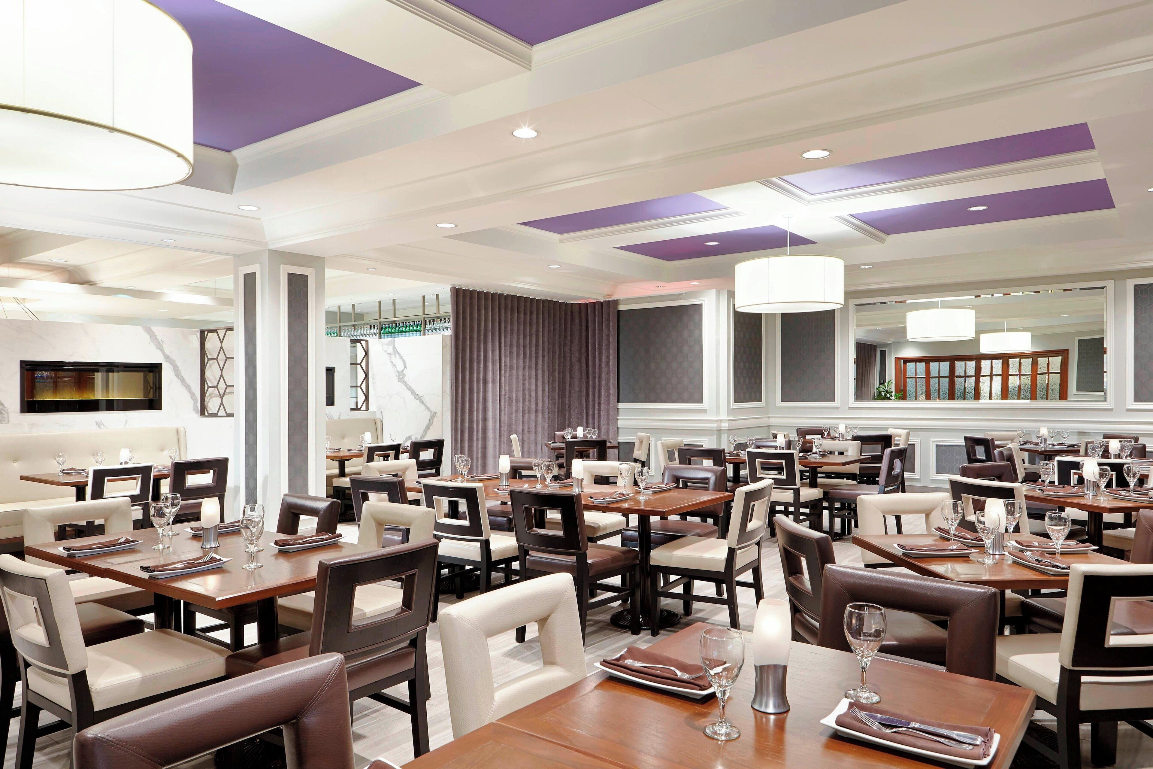 A spacious restaurant with multiple dining tables and chairs, featuring a modern ceiling design with purple accents.