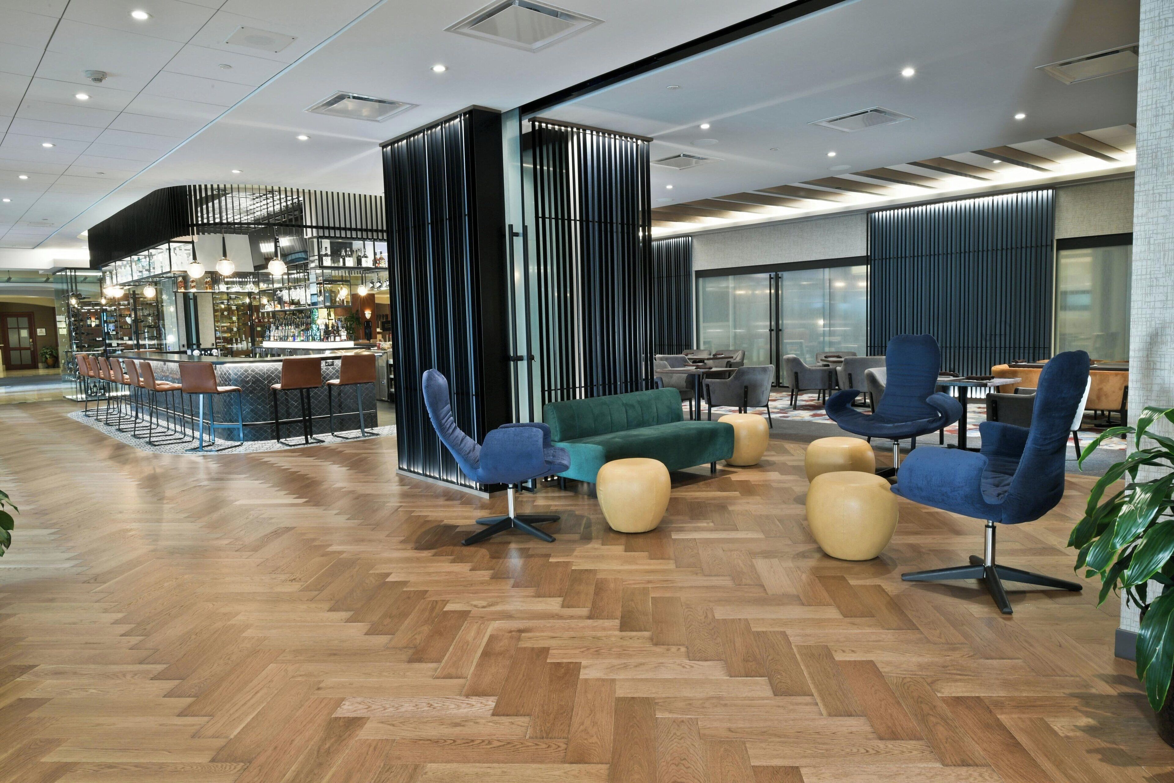 Un área de estar moderna con un bar, asientos y un piso de madera con patrón de espiga.