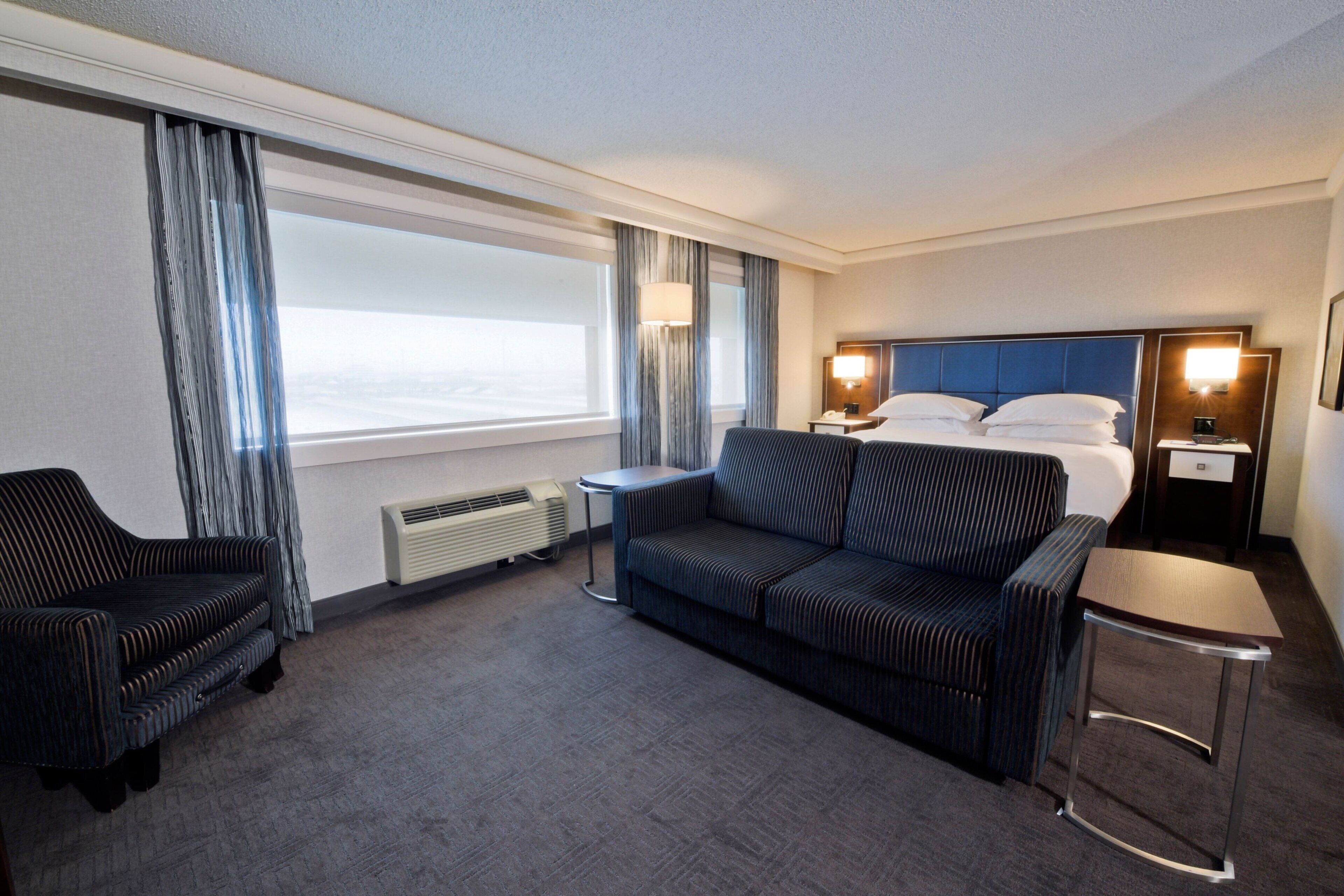 A hotel room with a large bed, a sofa, a chair, a small table, and a desk.