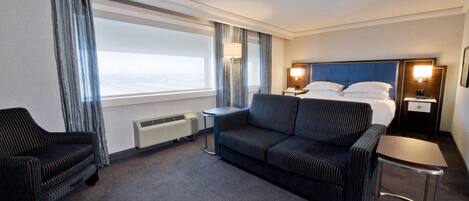 A hotel room with a large bed, a sofa, a chair, a small table, and a desk.