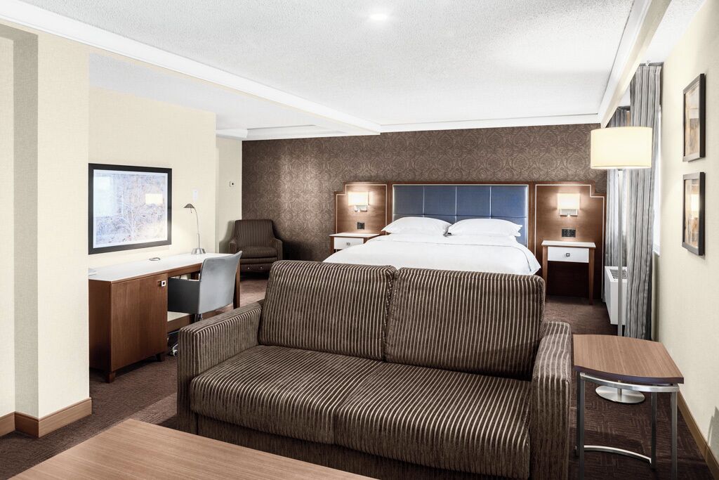 Una habitación de hotel con cama, escritorio, silla, sofá y televisor.