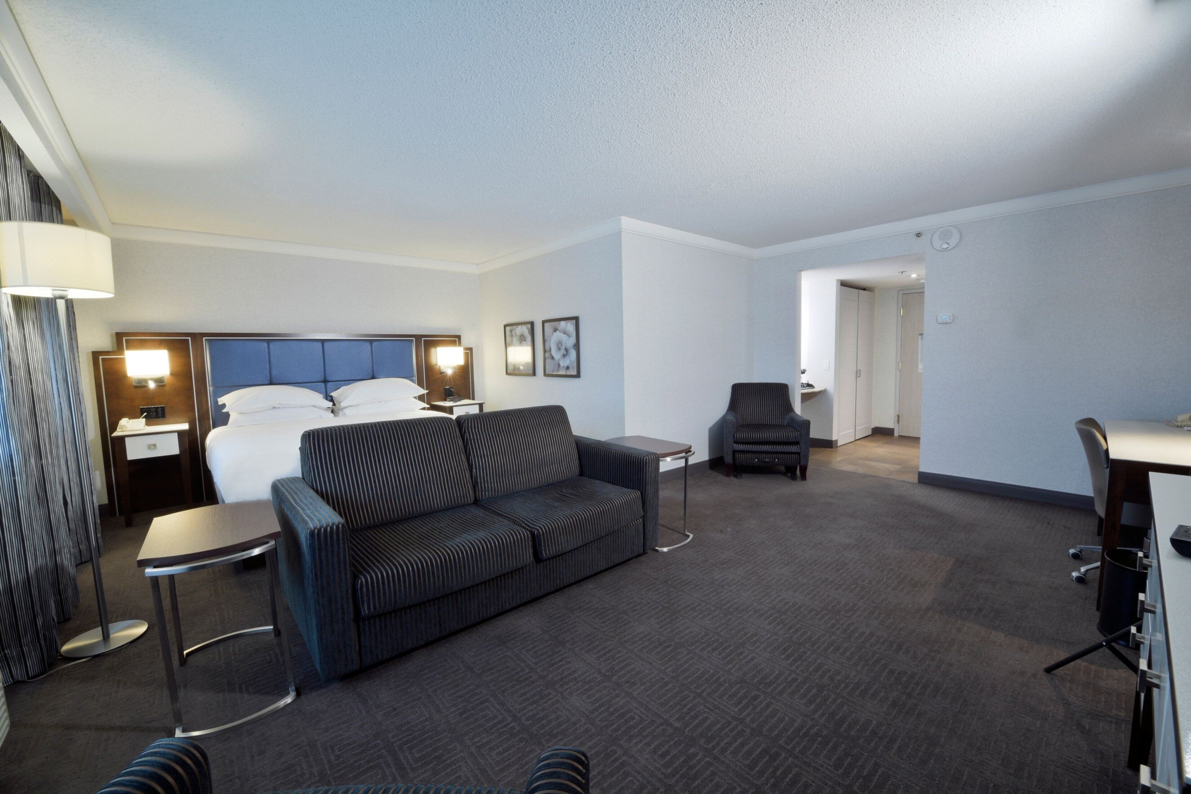 A hotel room with a bed, a sofa, a desk, and a chair.