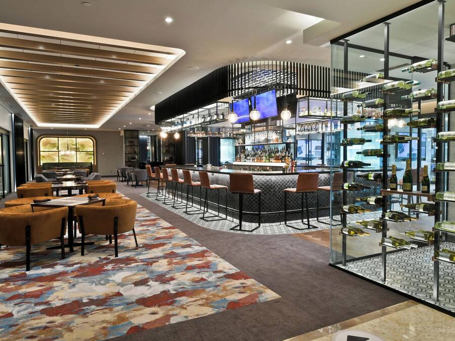 A modern bar area with a long counter, multiple seating options, and a wine display.