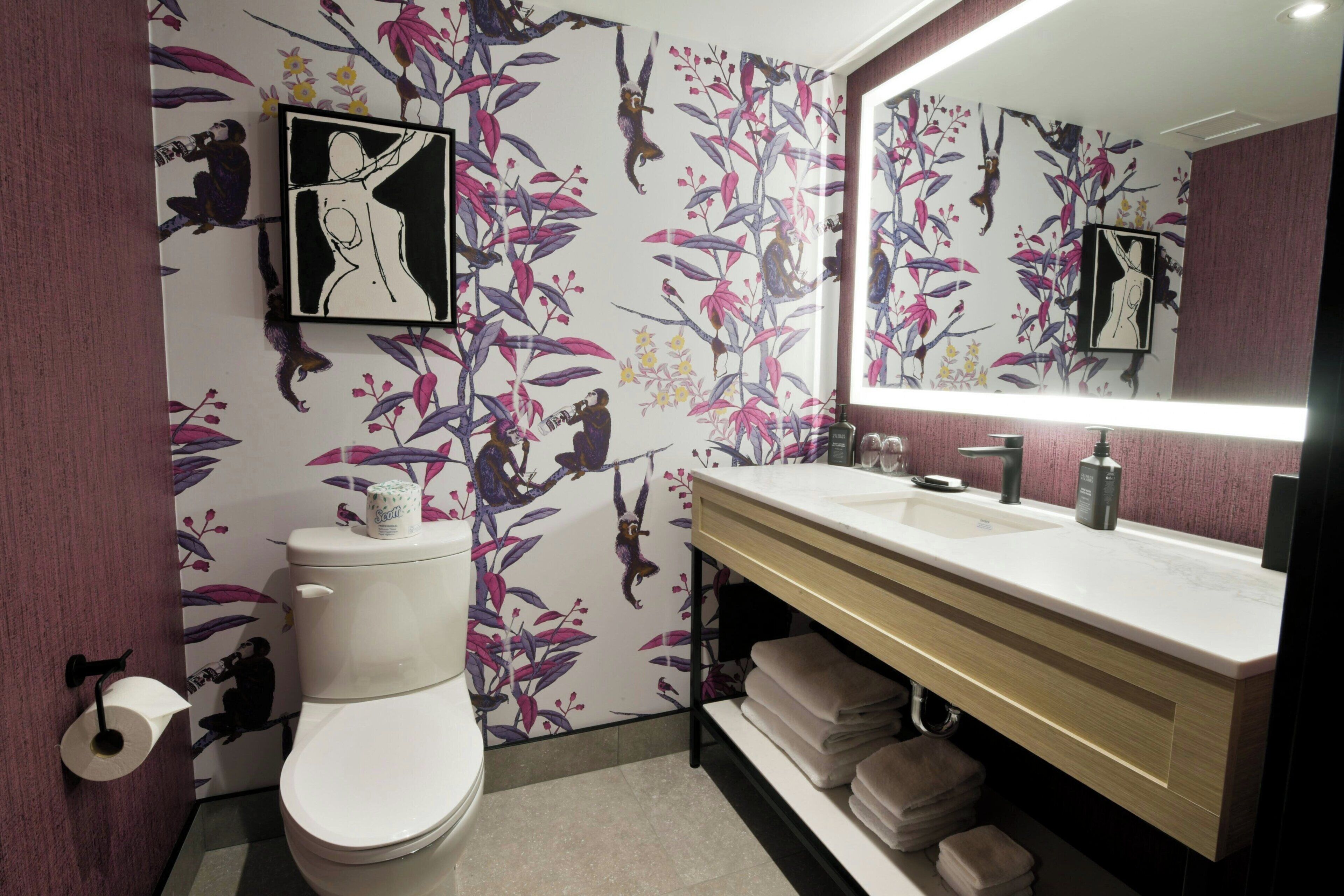 A bathroom with a floral wallpaper, a toilet, a sink with a mirror, and a towel rack.