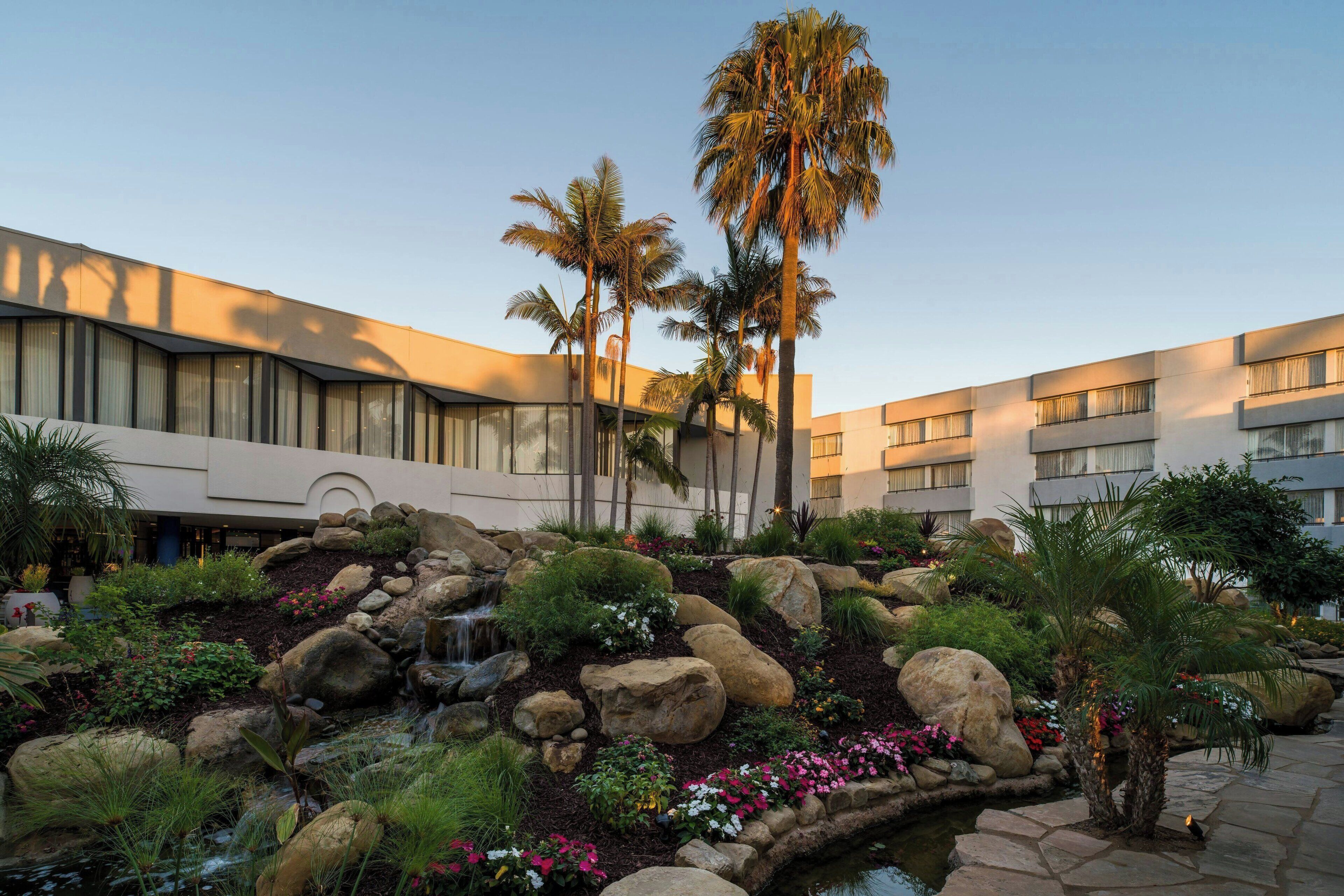 A hotel courtyard with a water feature, palm trees, and a stone pathway.