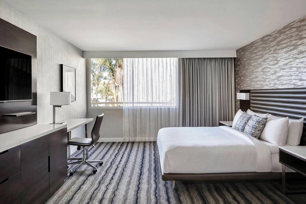 Une chambre d’hôtel moderne, dotée d’un grand lit, d’un bureau avec une chaise, d’une télévision et d’une fenêtre avec des rideaux.