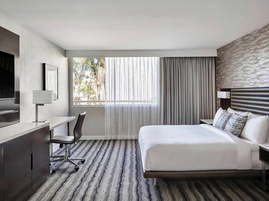 Une chambre d’hôtel moderne, dotée d’un grand lit, d’un bureau avec une chaise, d’une télévision et d’une fenêtre avec des rideaux.