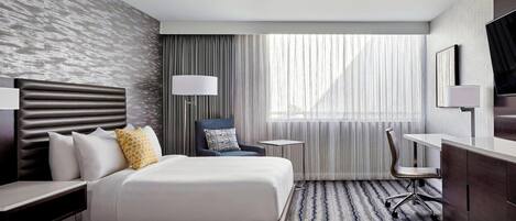 A hotel room with two beds, a desk, a chair, a TV, and a window with curtains.