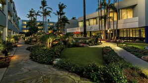 Un patio de hotel con un sendero de piedra, palmeras y una fuente de agua.
