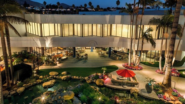 Un vestíbulo de hotel con una fuente central, palmeras y asientos al aire libre.